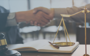 Two individuals shaking hands over a legal book, with a scale of justice in the foreground, symbolizing partnership and legal services in Michigan. This image represents the importance of professional relationships in Michigan web design for law firms.